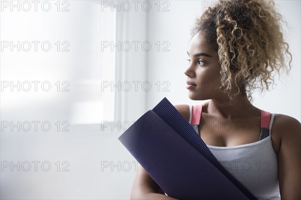 Pensive Mixed Race woman holding rolled up exercise mat