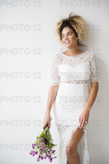 Mixed Race woman wearing wedding dress leaning on wall