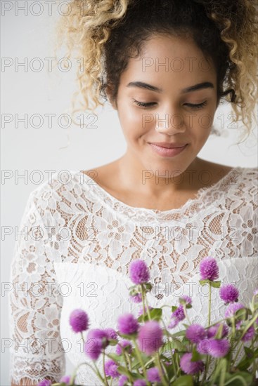 Mixed Race woman wearing wedding dress admiring bouquet