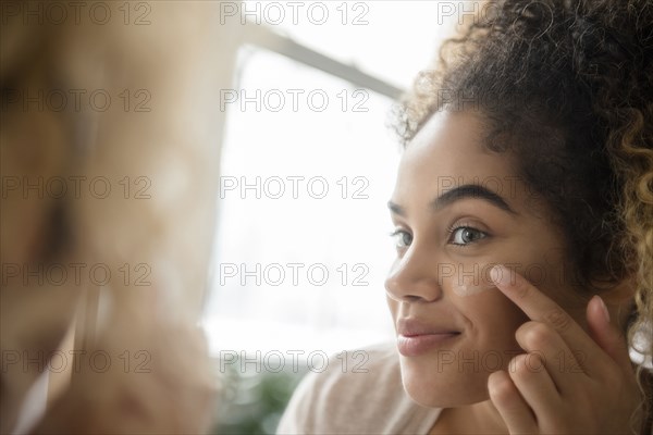 Mixed Race woman applying lotion to cheek