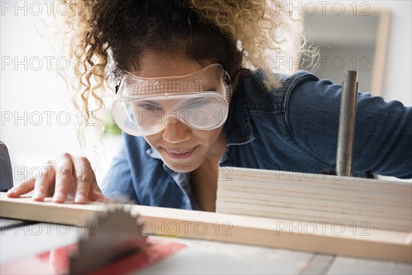 Mixed Race woman cutting wood with saw