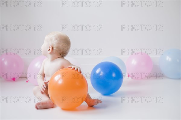 Caucasian baby boy sitting on floor with balloons