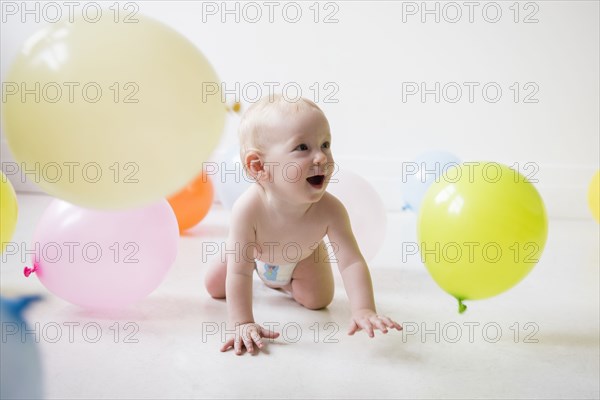Caucasian baby boy crawling on floor watching balloons