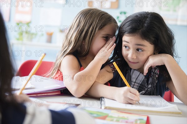 Girl whispering to classmate in school