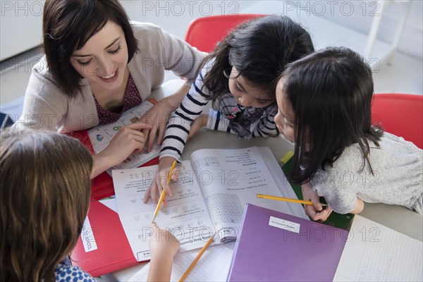 Teacher helping girls with workbook in classroom