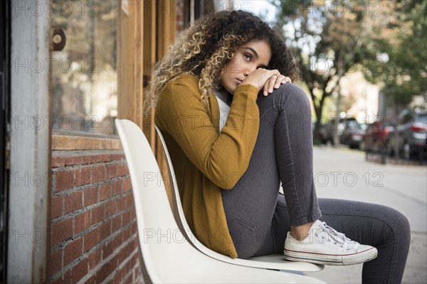 Pensive Mixed Race woman sitting on chair in city