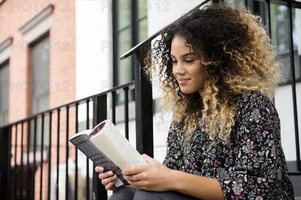 Mixed Race woman reading book in city