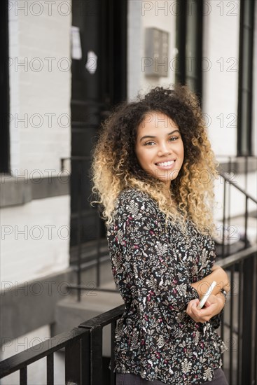 Smiling Mixed Race woman holding cell phone in city