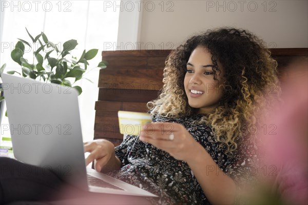 Mixed Race woman laying on bed online shopping with laptop