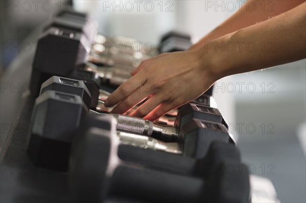 Hands of Mixed Race woman reaching for dumbbells