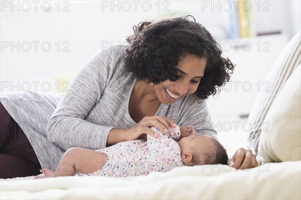Hispanic mother laying on bed playing with baby daughter