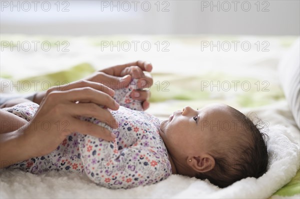 Hispanic mother holding hands with baby daughter on bed