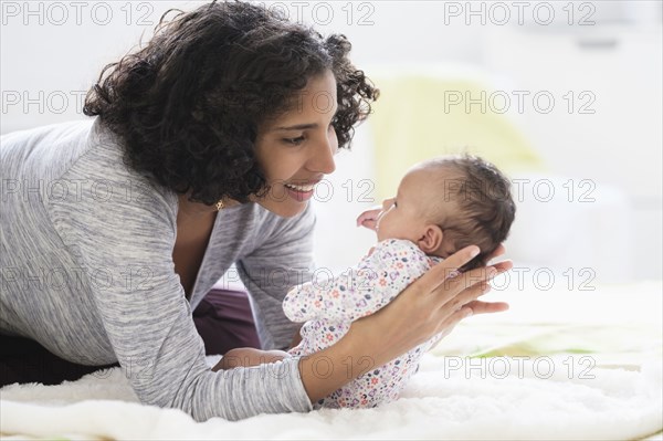 Hispanic mother laying on bed holding baby daughter