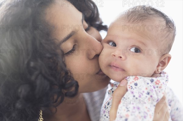 Hispanic mother kissing baby daughter on cheek