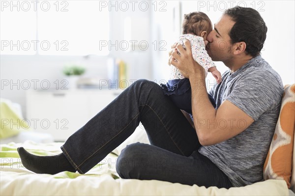 Hispanic father kissing baby daughter on cheek