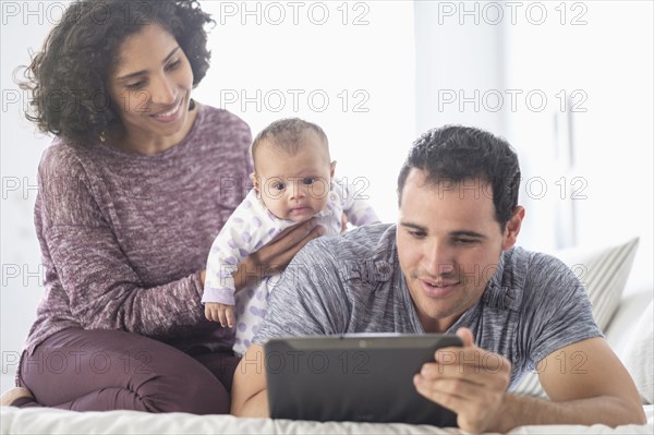 Hispanic mother and father with baby daughter watching digital tablet