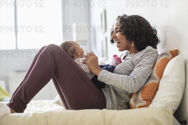 Hispanic mother playing with baby daughter on bed