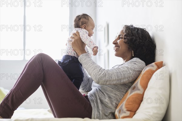 Hispanic mother playing with baby daughter on bed