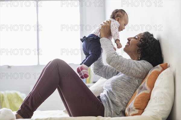 Hispanic mother playing with baby daughter on bed