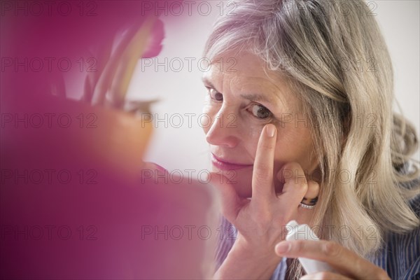 Caucasian woman applying cream to wrinkle near eye