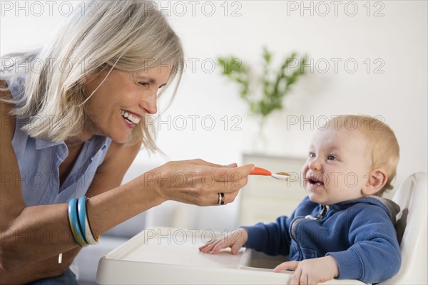 Smiling Caucasian grandmother feeding baby grandson in high chair