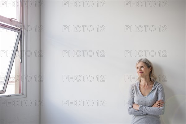 Smiling Caucasian woman leaning on wall near window