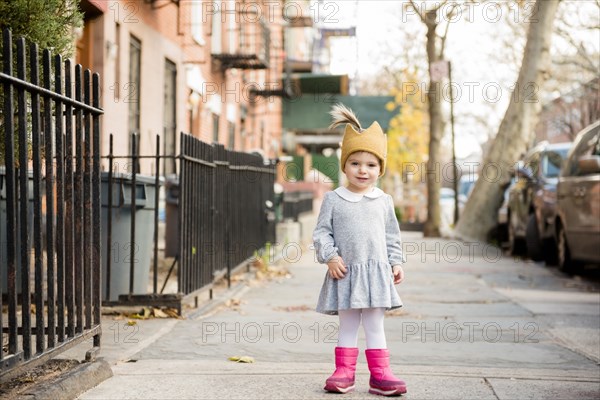 Smiling Caucasian baby girl wearing crown hat on city sidewalk