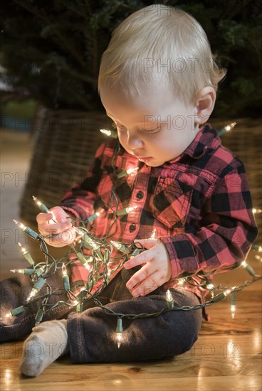 Caucasian baby boy sitting on floor wrapped in string lights