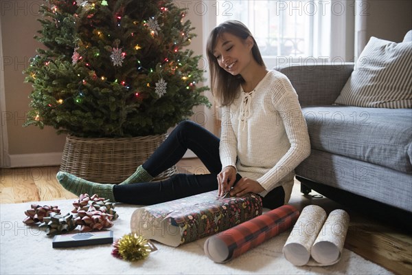 Mixed Race woman wrapping gift on floor near Christmas tree