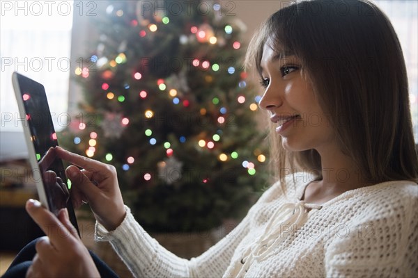 Mixed Race woman using digital tablet near Christmas tree