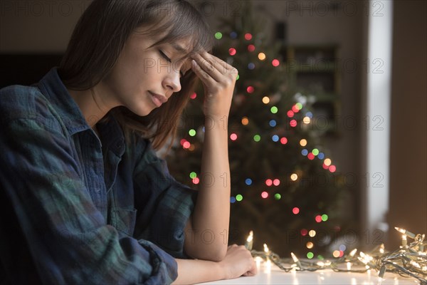 Mixed Race woman with headache near Christmas tree