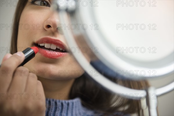 Mixed Race woman applying lipstick in mirror