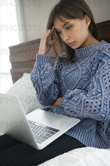 Frustrated Mixed Race woman using laptop in bed