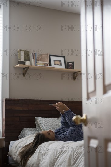 Mixed Race woman laying on bed texting on cell phone