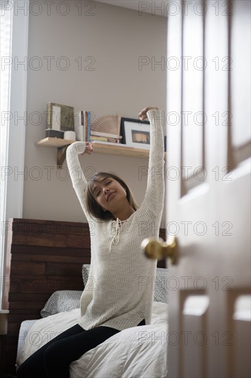 Mixed Race woman stretching arms on bed