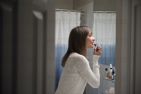 Mixed Race woman applying lipstick in bathroom