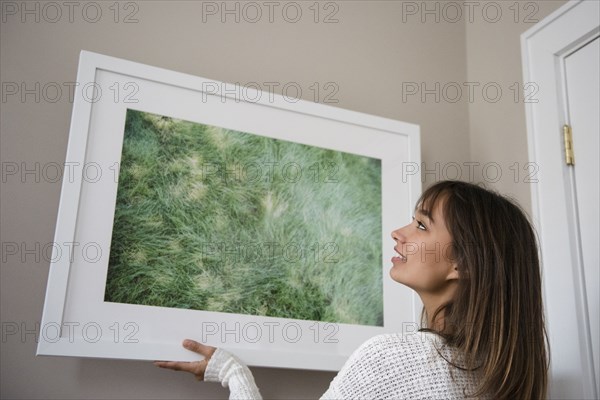 Mixed Race woman hanging picture frame on wall