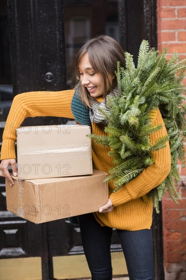 Mixed Race woman carrying pine wreath and cardboard boxes