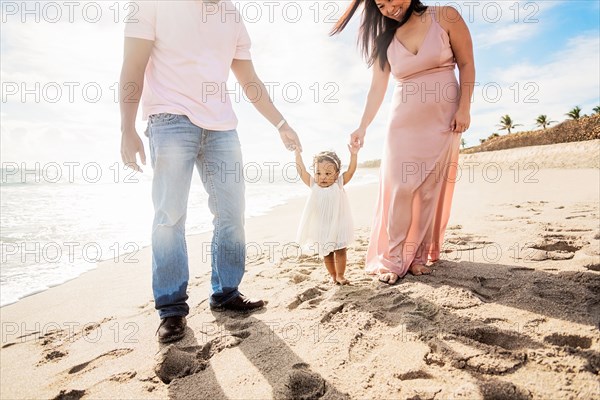 Couple holding hands of baby daughter walking on beach