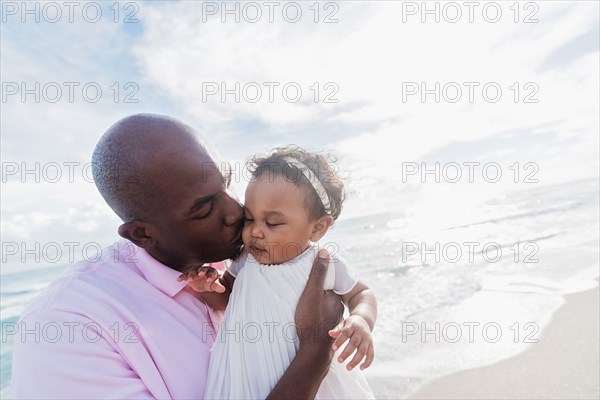 Father kissing cheek of baby daughter on beach