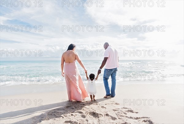 Couple holding hands of baby daughter walking on beach