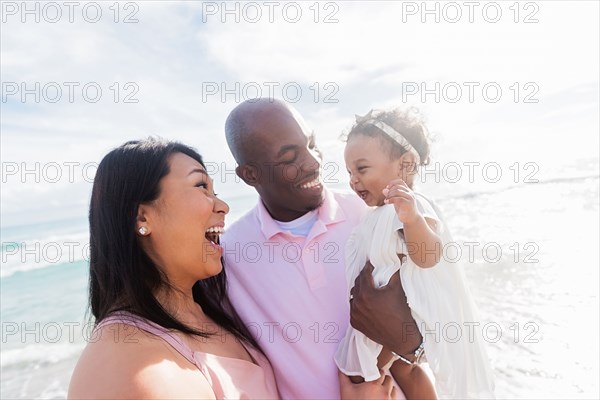 Couple laughing with baby daughter near ocean