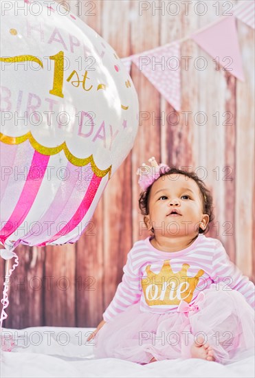 Mixed Race baby girl sitting near birthday balloon