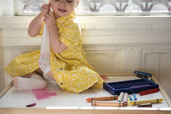 Caucasian baby girl sitting near window removing sock