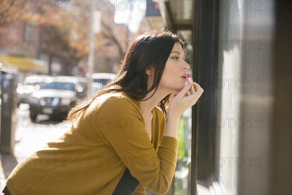 Caucasian woman applying lipstick in city