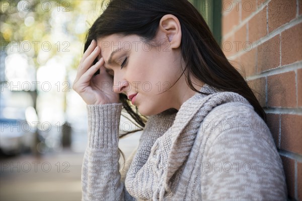 Caucasian woman with headache leaning on brick wall