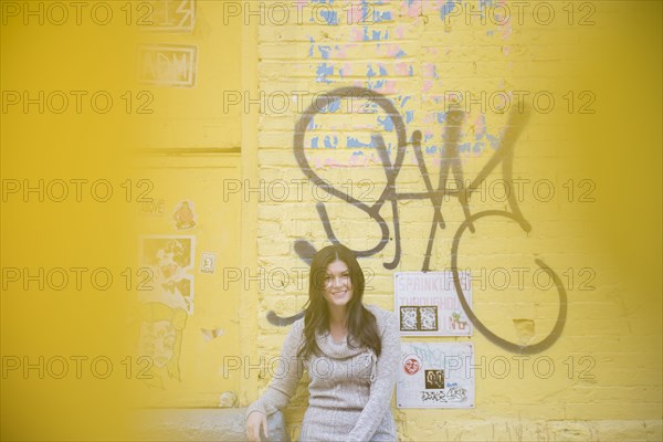 Caucasian woman leaning on yellow graffiti wall