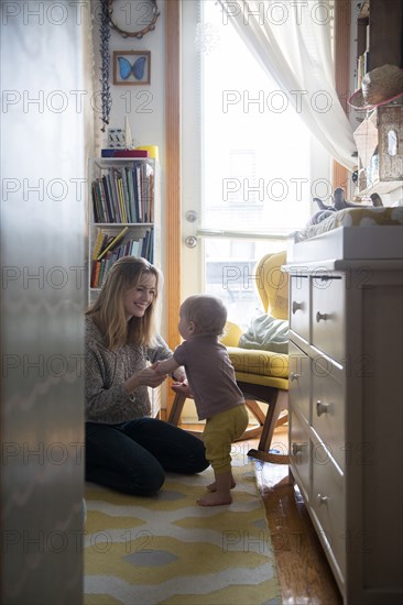 Smiling mother helping baby son walking