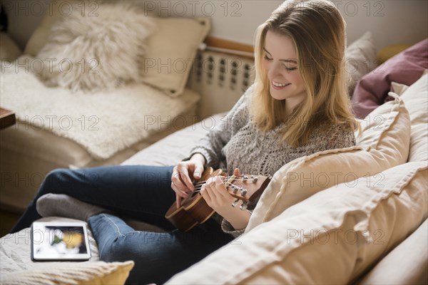 Smiling woman sitting on sofa playing ukulele