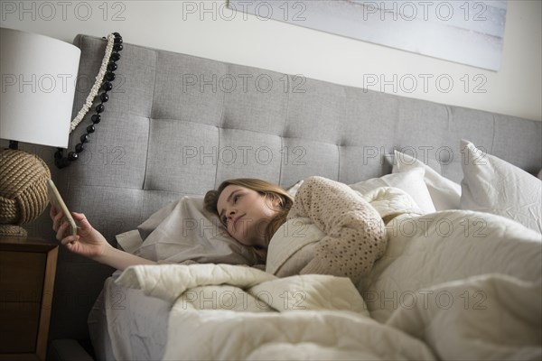 Woman laying in bed texting on cell phone